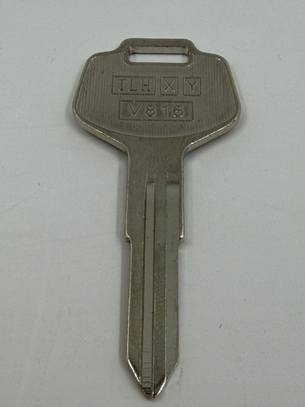 A single metal key with stamped letters 'TLH X Y' and numbers 'M818' on the bow, shown on a plain light gray background.